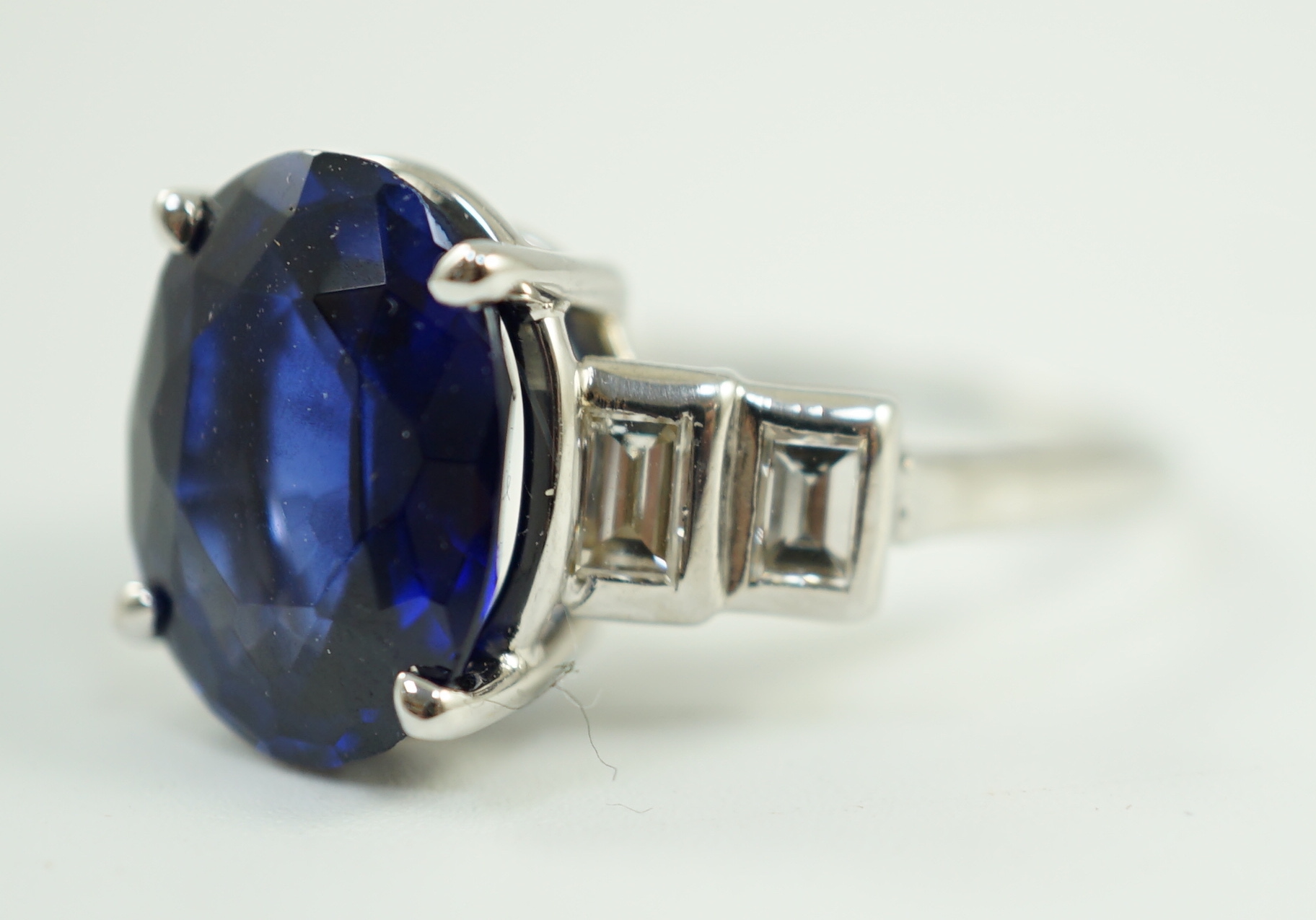 A platinum and single stone oval cut sapphire set cocktail ring, with graduated four stone baguette cut diamond set shoulders